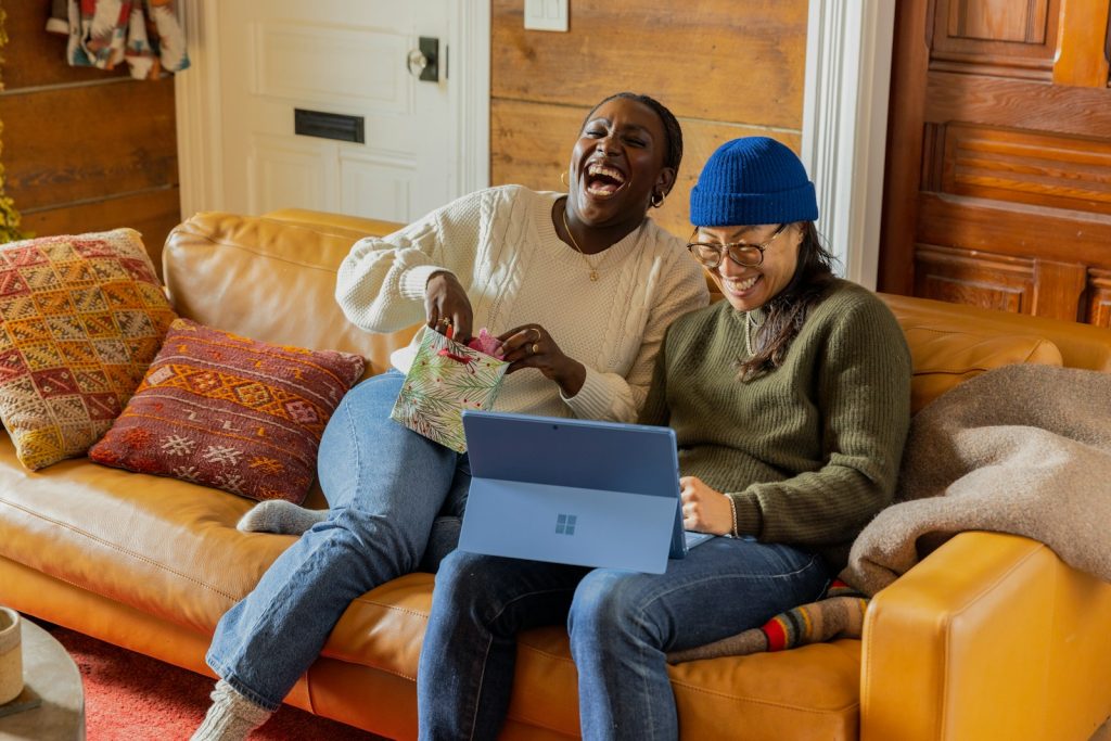 Duas pessoas sentadas com um notebook no colo, sorrindo. Imagem para representar a ação de fundo de funil - ou seja, a decisão de compra.